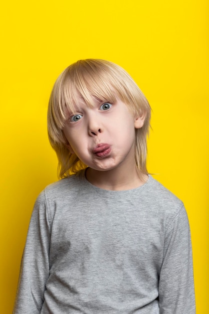 Funny fair-haired boy shows tongue and makes grimace. Vertical frame.