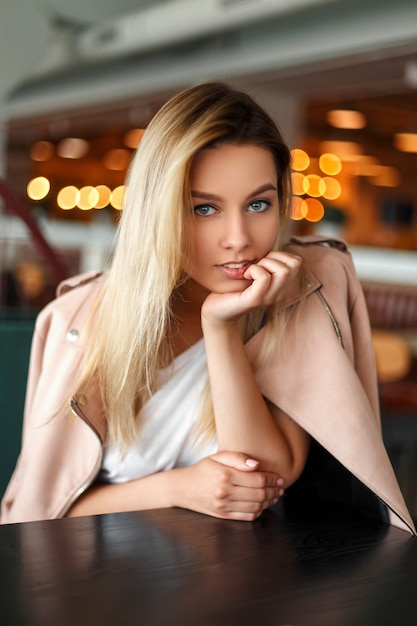 Funny fashionable beautiful woman in a fashion pink jacket sits in a cafe