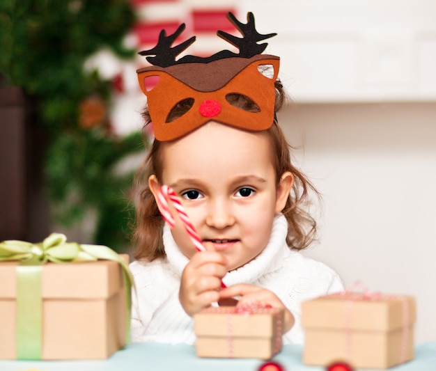 Funny girl in a Christmas deer mask holding candy cane in a hand