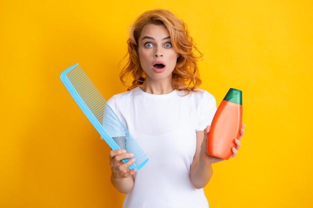 Funny girl combing hair Redhead woman with a comb isolated on yellow background Woman hold bottle