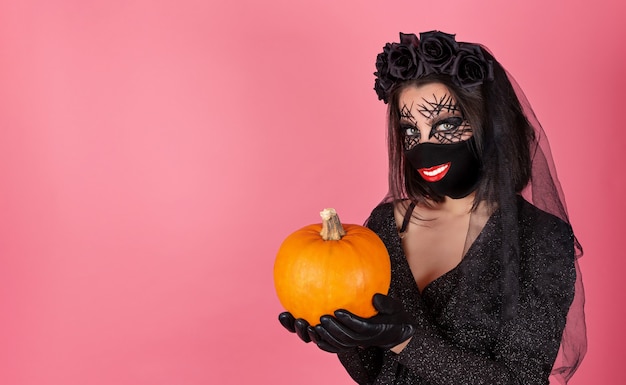 Photo funny girl in a halloween costume with a smile print on a black mask and a pumpkin in her hands