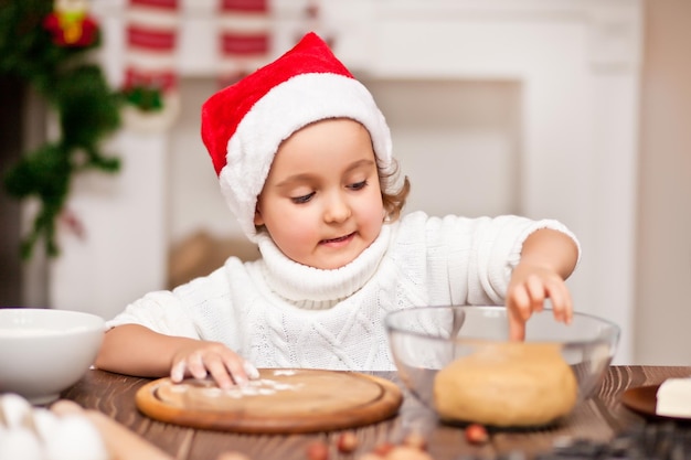 Funny girl in a Santa cap baking christmas cookies at home