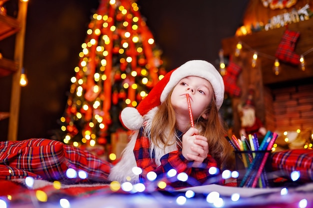 Funny girl in Santa hat dreaming writes letter to Santa