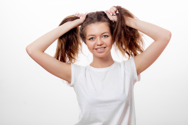 Funny girl in white t-shirt making two ponytails with her brown hair