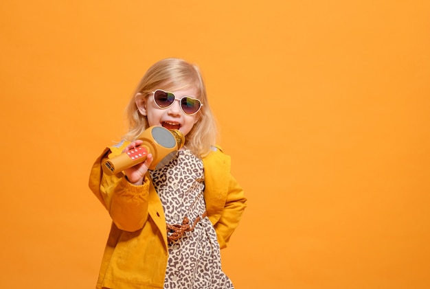 Funny girl in yellow clothes on yellow with microphone in hand