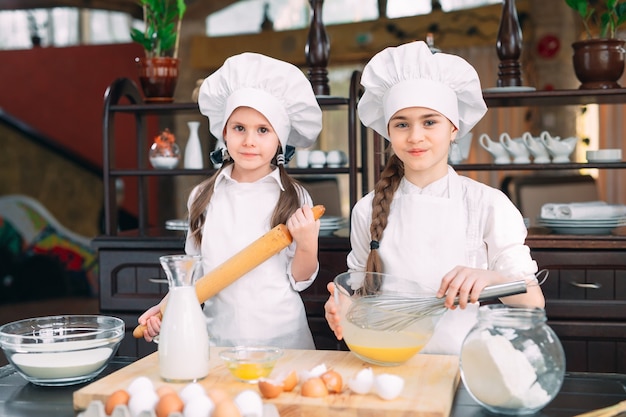 Funny girls kids are preparing the dough in the kitchen.