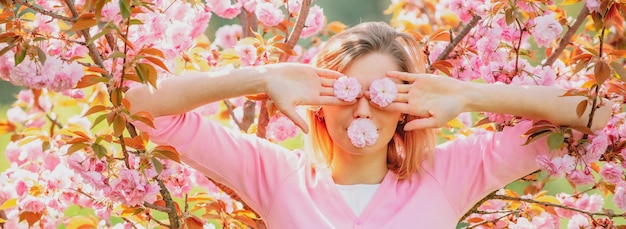 Funny girls with blooming sakura cherry flover closing eyes with flovers hides eyes march womens day...