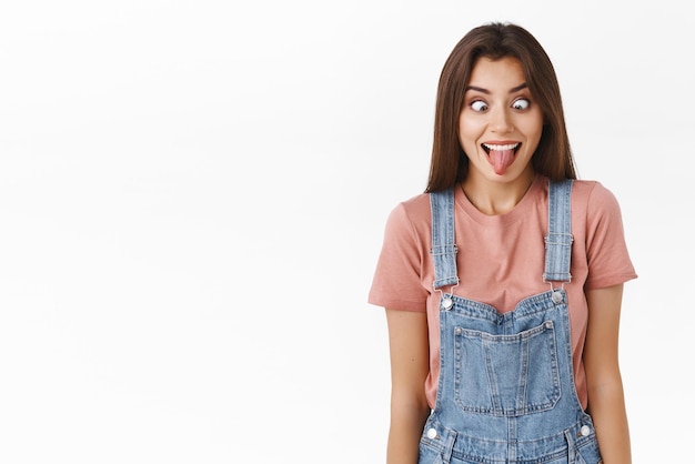 Funny and goofy carefree silly girl having fun entertain friends showing hilarious faces stick tongue and squinting shifting eyes and smiling like crazy clown standing white background