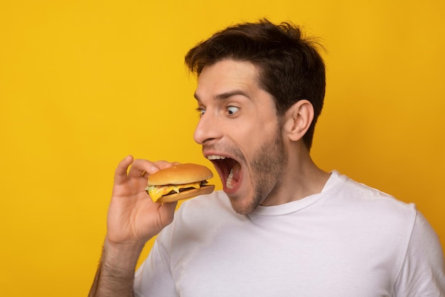 Funny guy holding burger biting sandwich at studio