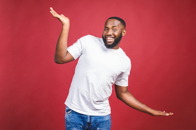 Funny guy in white t-shirt jumping and looking at camera. Studio portrait of emotional african male model posing on red background.