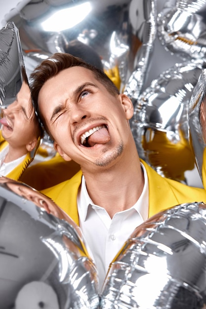 Funny guy with a lot of silver air balloons fooling around at birthday party