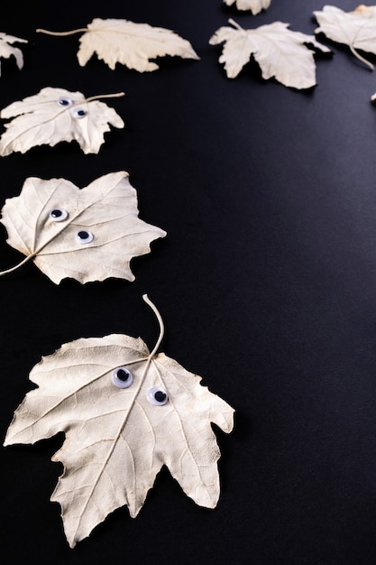 Funny Halloween concept. Autumn leaf with eyes like a ghost  on black  background. Top view, flat lay