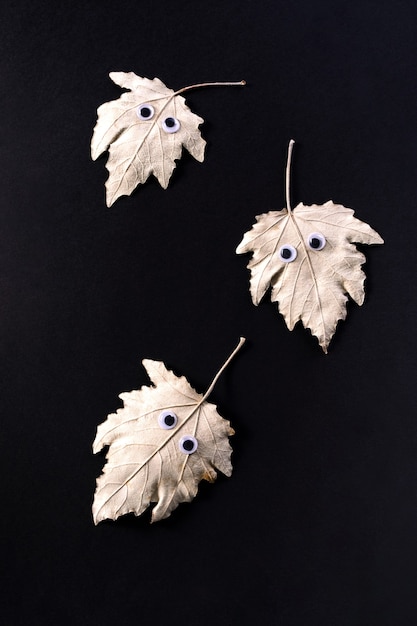 Funny Halloween concept. Autumn leaf with eyes like a ghost  on black  background. Top view, flat lay