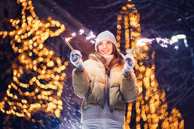 Funny happy caucasian girl burns sparklers by holiday illumination on new years eve