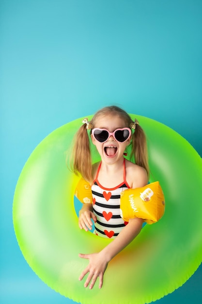 Funny happy child in bright swimsuit and sun glasses smiling and holding a swimming ring