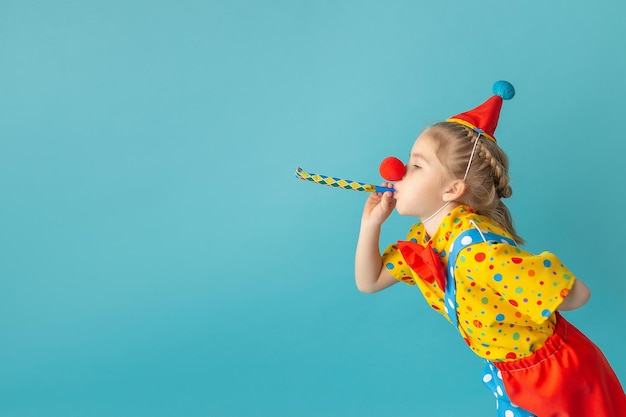 Funny kid clown against blue background Happy child playing with festive decor Birthday concept