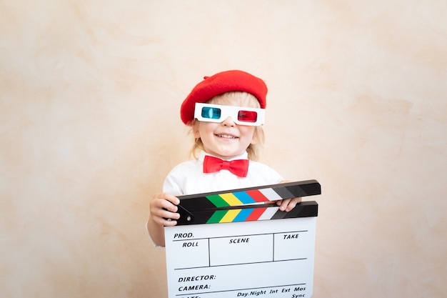 Funny kid holding clapper board. Happy child having fun at home. Retro cinema concept