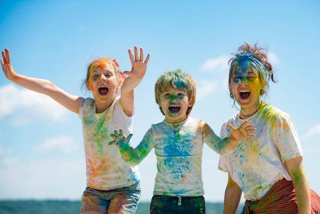 Funny kids face in color splash coloured powder on children body cheerful friends showing hands pain...