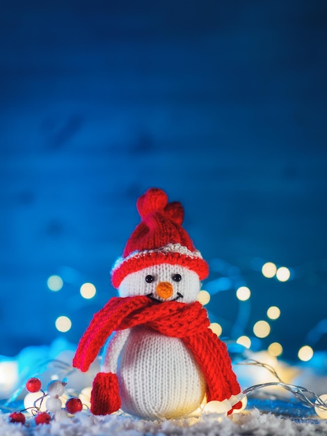 Funny knitted toy snowman Christmas decor fake snow decoration bokeh garlands blue background