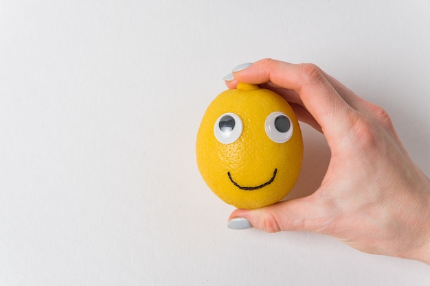 Funny lemon with eyes and smile on white. Woman's hand holding a lemon-smile.