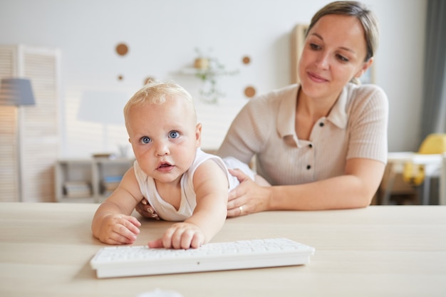 Funny little baby trying to play with computer keyboard while his mother holding him, horizontal shot