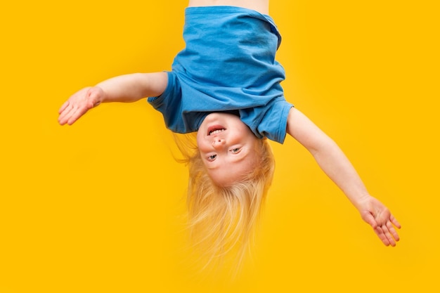 Funny little blonde girl upsidedown on bright yellow background Child topsyturvy Copy space