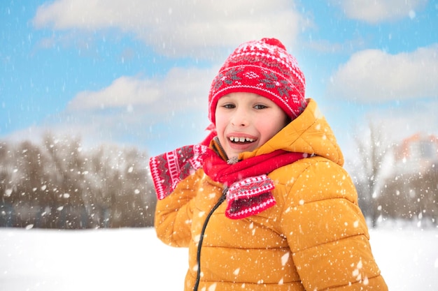 Funny little boy in colorful clothes playing outdoors during a snowfall