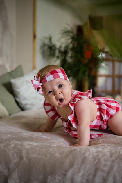 Funny little girl in a bodysuit with a bandage on her head crawls on the bed in the room