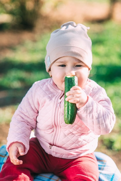 Funny little girl eating fresh cucumber in the garden in spring