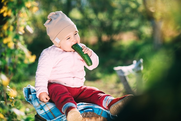 Funny little girl eating fresh cucumber in the garden in spring