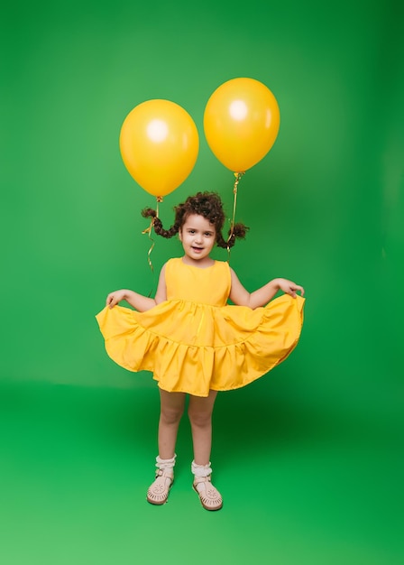 Funny little girl on a green background A girl is having fun with yellow balloons balloons lift up the pigtails of the child