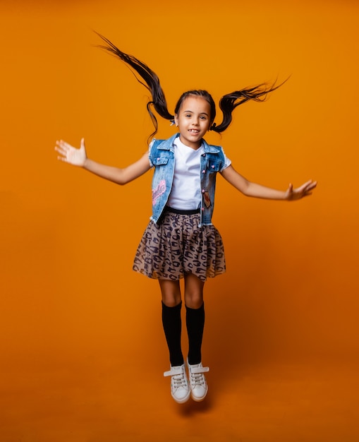 Funny little girl jumping and having fun on a colored yellow background.