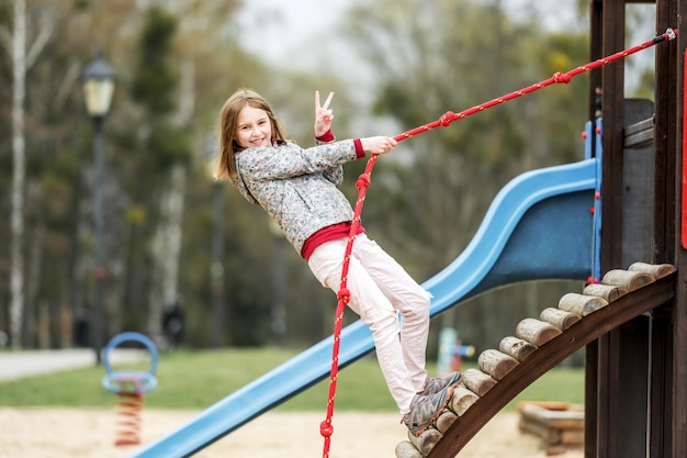 Funny little girl playing on the playground with rope