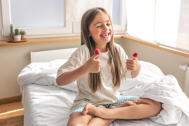 Funny little girl with raspberries on her fingers in bed in the morning