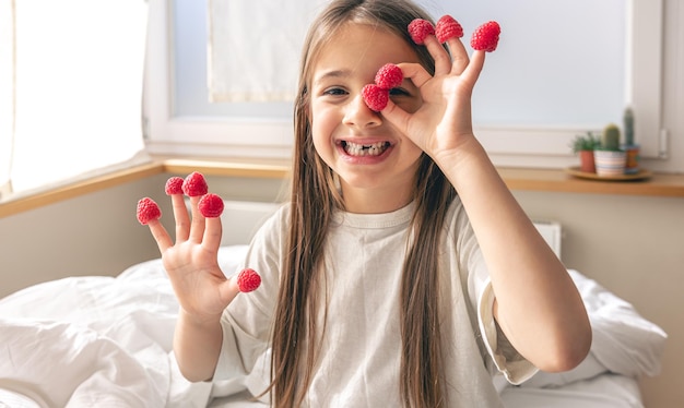 Funny little girl with raspberries on her fingers in bed in the morning