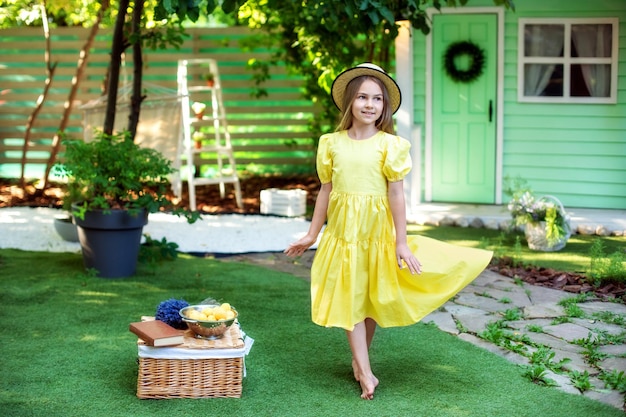 funny Little girl in yellow dress and straw hat sitting on lawn at summer at home.