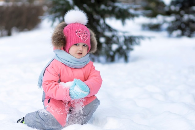 Funny little toddler girl playing in snowballs. wintertime winter game for children. Kid having fun Christmas time