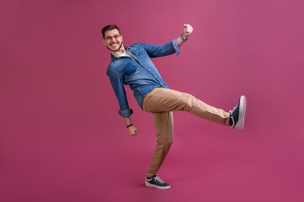 Funny man in casual is having some fun. He is posing and dancing. Isolated on pink background.