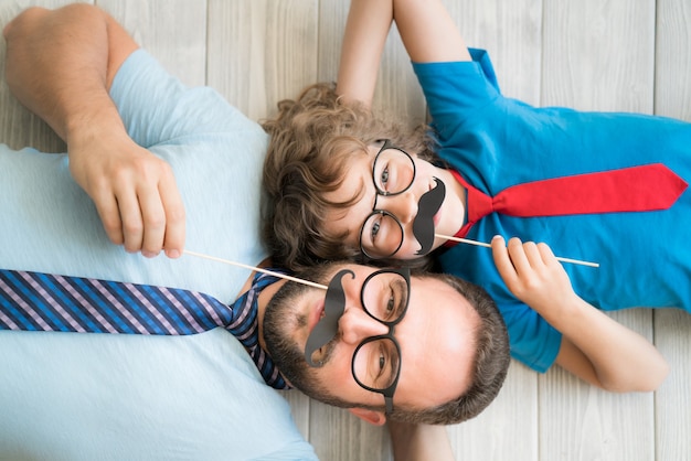 Photo funny man and kid with fake mustache. happy family playing in home