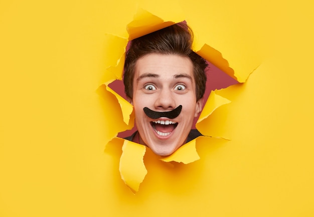 Funny man with mustache looking through torn paper hole