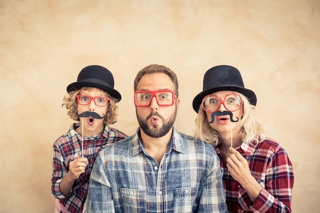 Funny man, woman and kid with fake mustache. Happy family playing in home