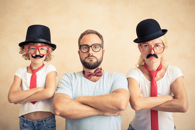 Funny man, woman and kid with fake mustache. Happy family playing in home