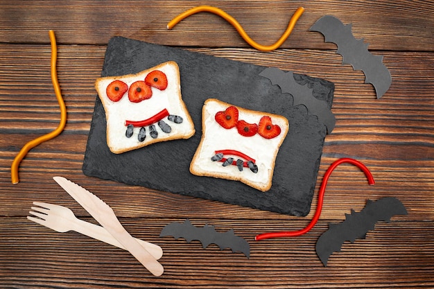 Funny monster face on halloween sandwich toast bread with butter strawberry sweetscutting serving boardbats on black background close up Kids child sweet dessert breakfast lunch food