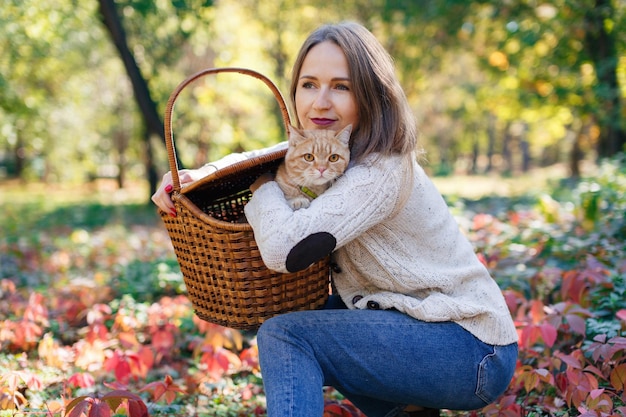 Funny pet on walk outdoors healthy young cat in picnic wicker basket with woman caring for a cat