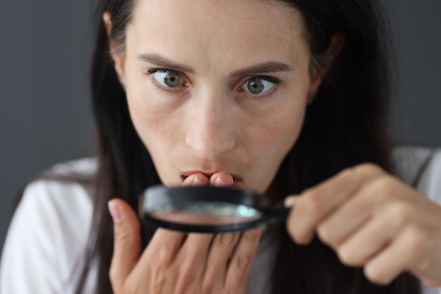 Funny picture of young surprised girl looking at camera through magnifying glass search for new