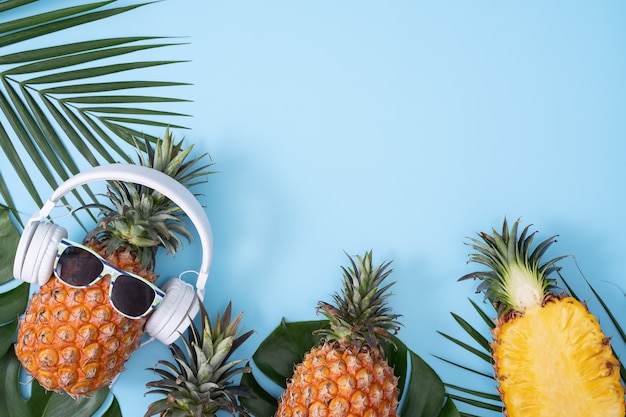 Funny pineapple wearing white headphone with tropical palm leaves