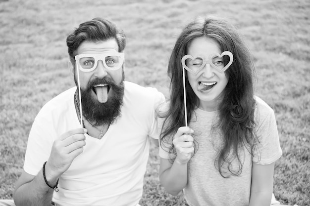 Funny and playful Funny couple looking through prop glasses on green grass Bearded man and sexy woman making funny grimace on summer day Enjoying funny photo booth