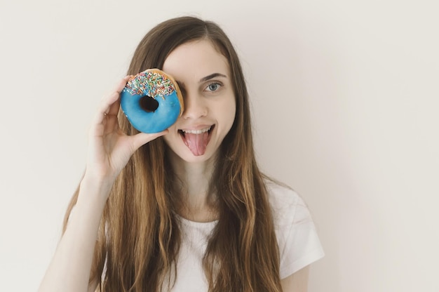 Funny portrait of young European woman holding a blue donut with sprinkles