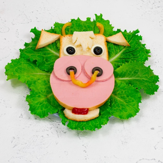 Funny sandwich with edible bull symbol of 2021 made of toast sausage and egg on green lettuce leaves Closeup Breakfast idea for children New Year Christmas food top view holiday holiday culinary arts