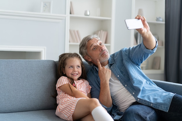 Funny selfie with dad. Self portrait of father and his little daughter taking selfie while sitting on the sofa.